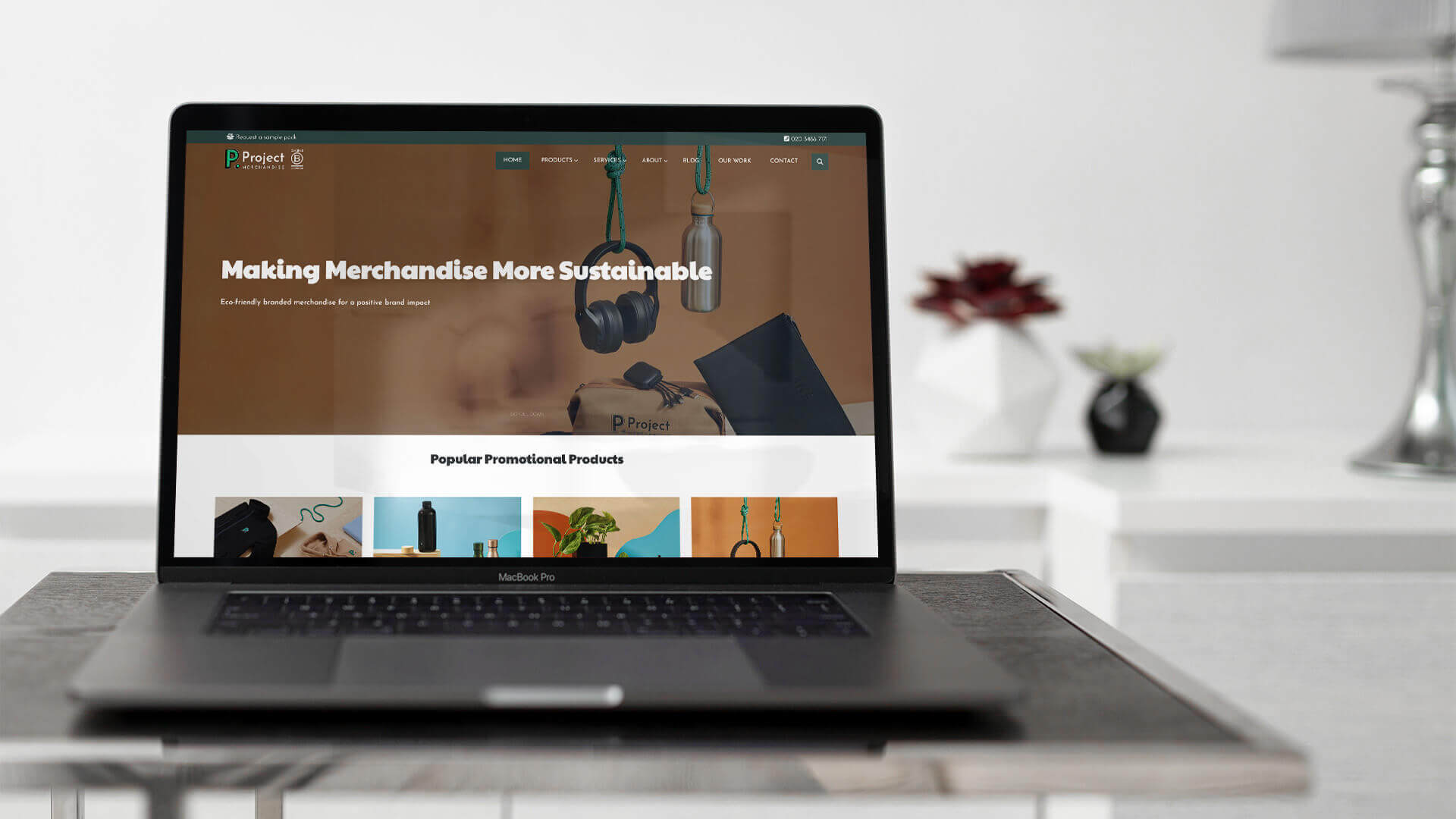 Project Merchandise homepage on a laptop, with the headline Making Merchandise More Sustainable above a row of popular promotional products