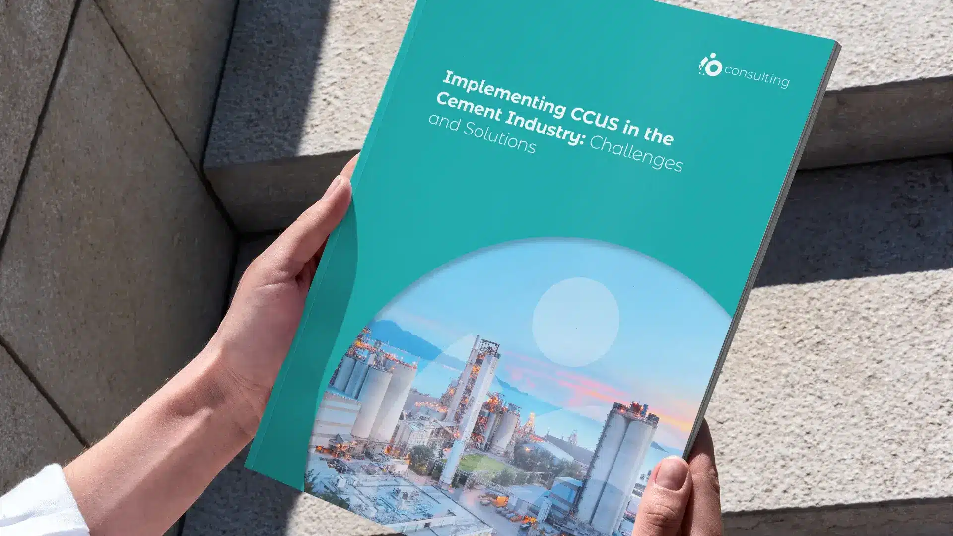 A teal report cover titled Implementing CCUS in the Cement Industry, held up in front of a concrete building